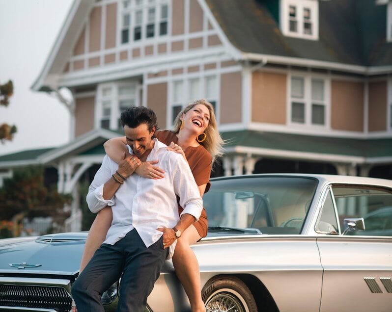 A couple poses on a vintage car.